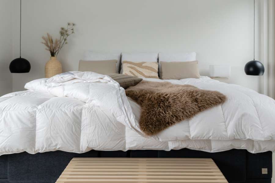 Chambre minimaliste scandinave avec une housse de couette blanche, jetés de lit beiges et coussins décoratifs sur base de lit noire