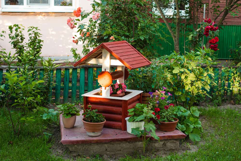 Un chemin pavé traverse un jardin luxuriant avec des parterres de fleurs colorées, des bancs en bois, et des maisons en arrière-plan, évoquant l'idée d'un jardin urbain bien entretenu