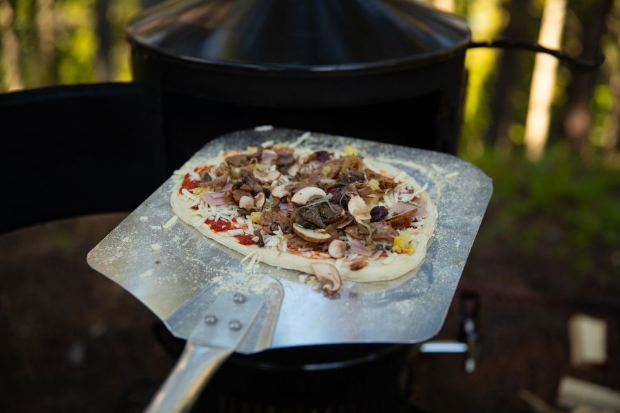 Pizza sur une pelle avant d’être cuite dans un four à bois extérieur, prête à être mise dans la chaleur du four