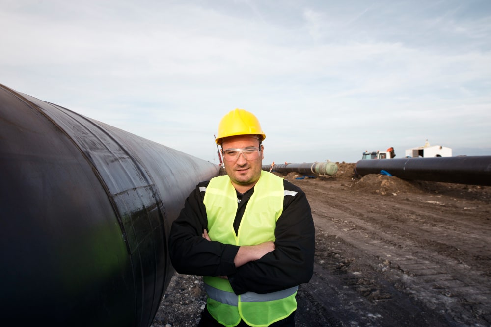 Un professionnel en gilet de sécurité devant une grande conduite, prêt pour tout projet, même un remplacement d'une fosse septique.