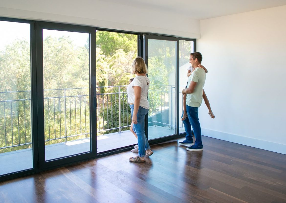 Un nouveau départ pour construire à Vitré. Famille dans un appartement neuf avec de grandes baies vitrées, se projettant dans l'avenir et le projet de construire à Vitré.