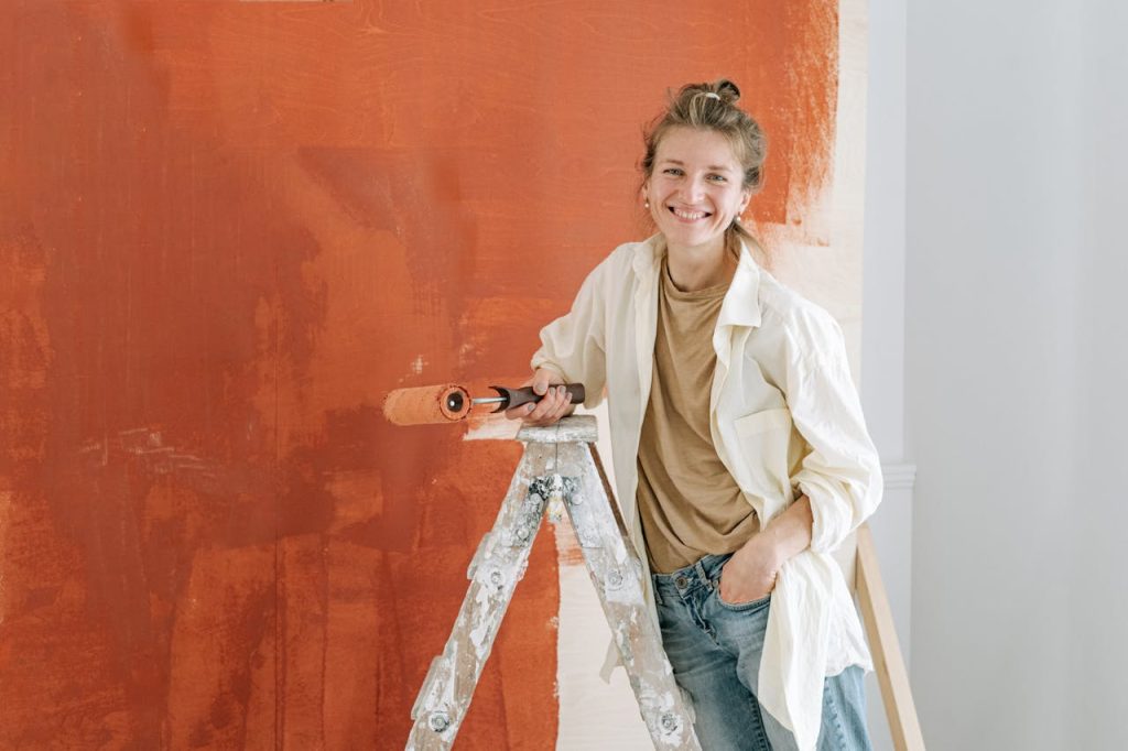 Femme souriante avec rouleau de peinture, prête à peindre une façade ancienne ou un mur intérieur en rénovation.