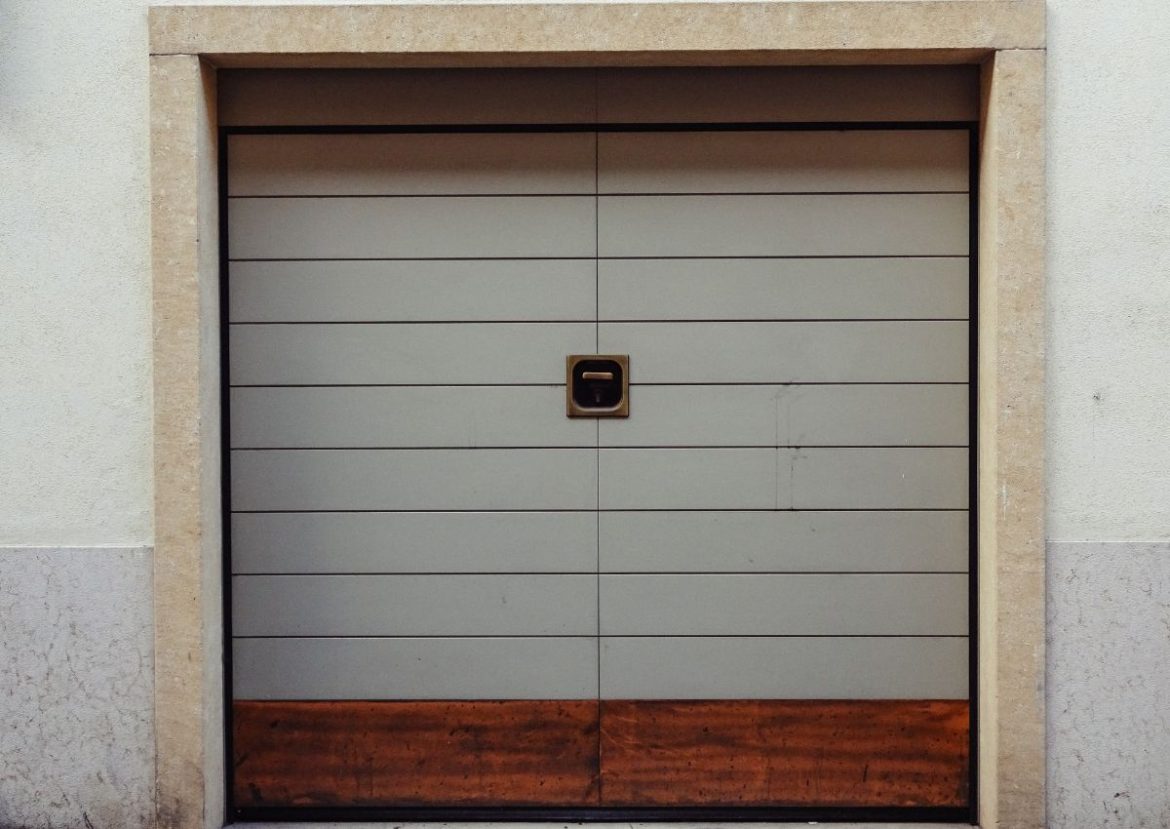 Porte garage battante contemporaine avec poignée centrale. Photographie frontale d'une porte garage battante moderne, bicolore, encadrée de pierre claire.
