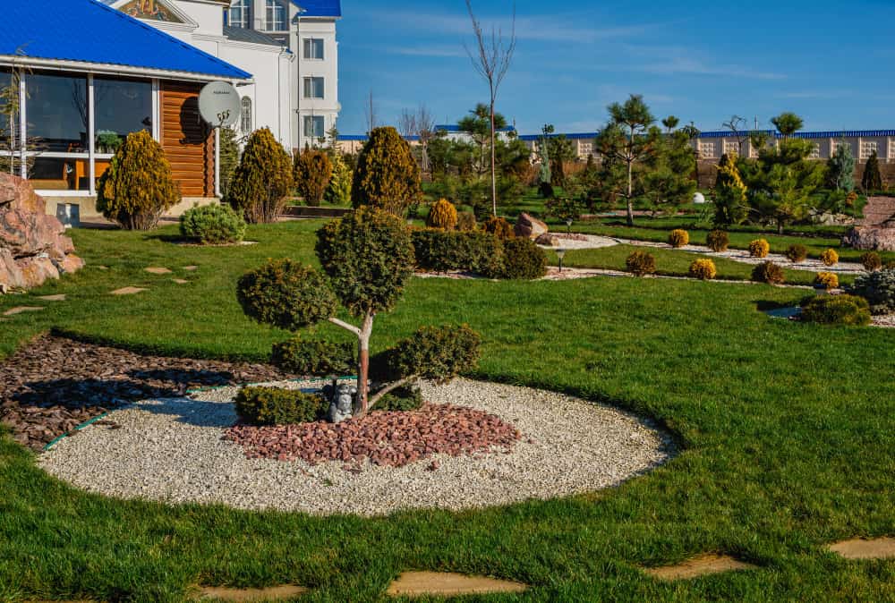 Grand jardin paysager avec des arbustes taillés et des zones de paillage minéral.