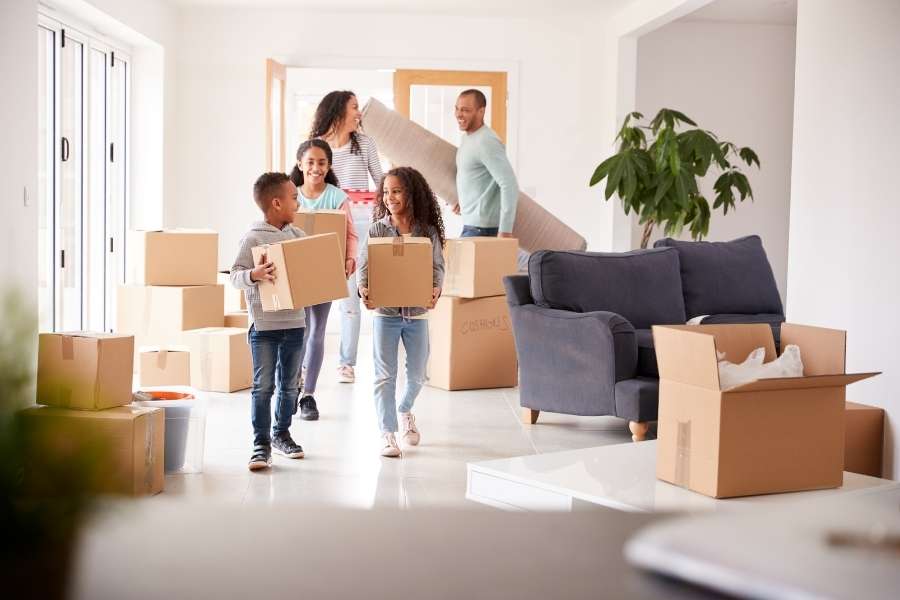 Une famille souriante porte des cartons et un tapis dans un grand salon lumineux lors d'un déménagement paris.