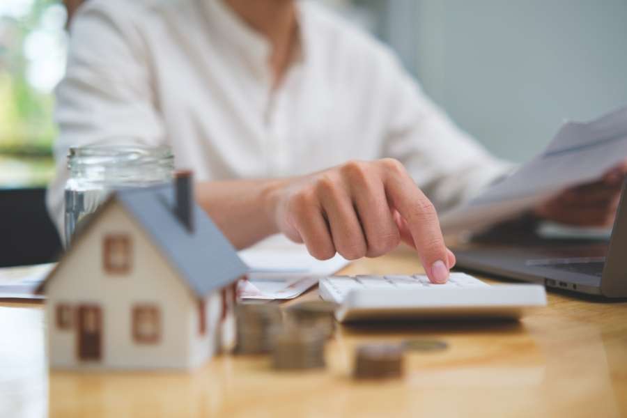 Une personne utilise une calculatrice pour valoriser votre bien immobilier avec une maquette de maison en premier plan.