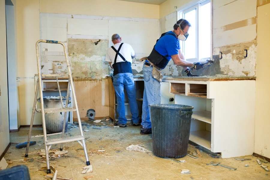 Deux ouvriers en plein chantier de démolition pour une rénovation lourde à Montpellier dans une cuisine en travaux.