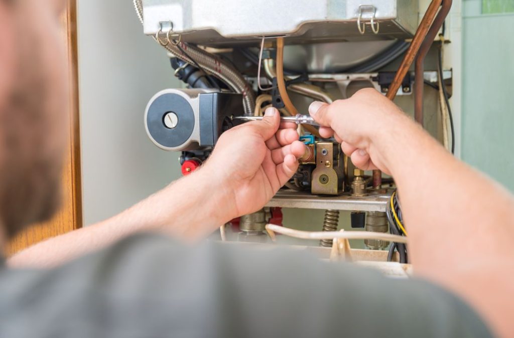 Un technicien utilise un tournevis sur la chaudière pour régler un problème d’arrêt de circulateur de chauffage.
