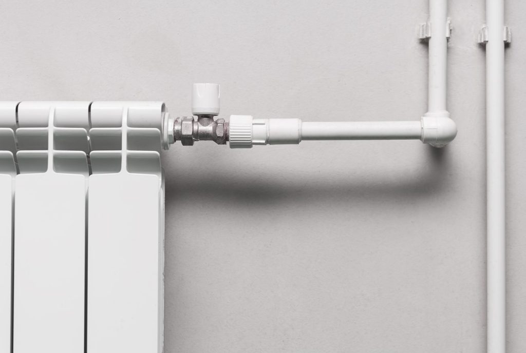 Un radiateur blanc équipé d'une vanne thermostatique et de sa tuyauterie, souvent à l'origine d'un bruit dans les tuyaux de chauffage.