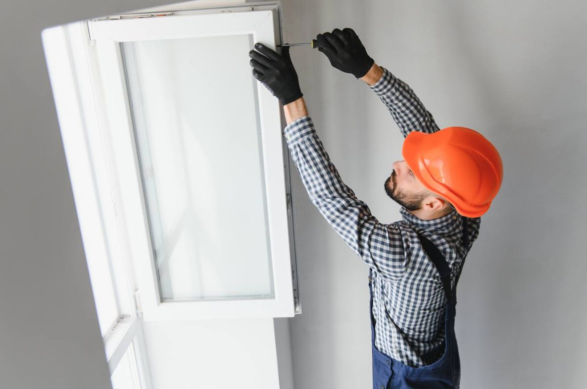 Un artisan en tenue de travail et casque orange installe une fenêtre blanche en PVC, une prestation détaillée dans un exemple devis detaille menuiserie pvc pose comprise