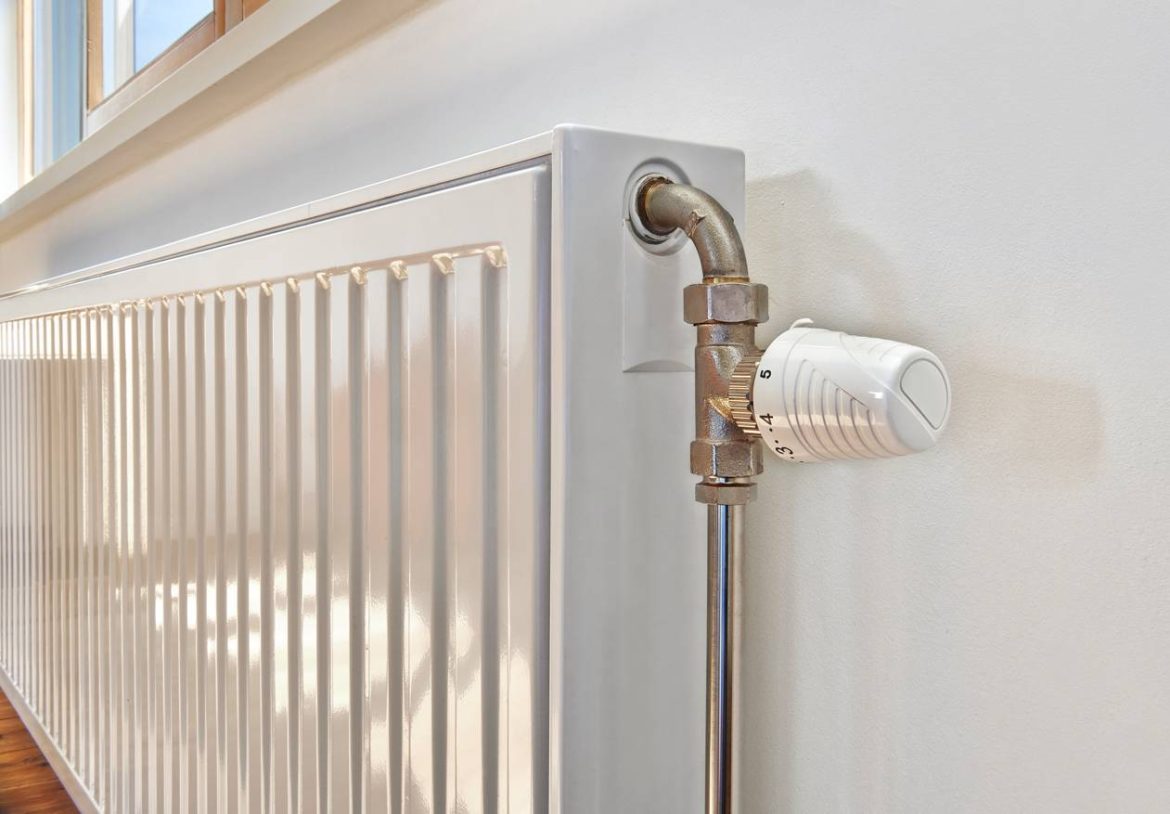 Un radiateur blanc et sa tuyauterie murale pour comprendre l'origine d'un bruit dans les tuyaux de chauffage